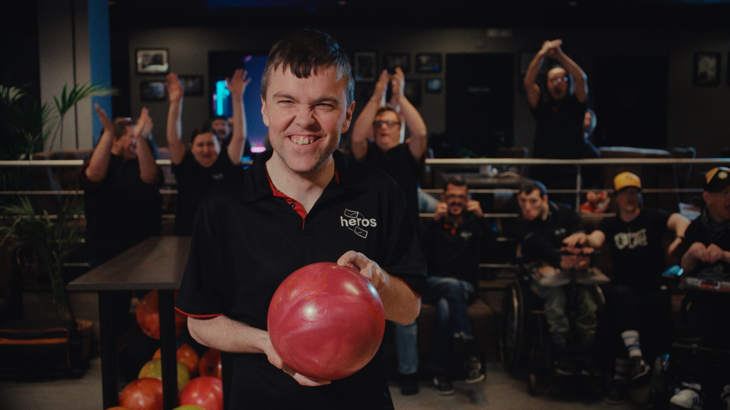 En kille som håller ett bowlingklot. Bakom honom jublar hans lagkompisar.